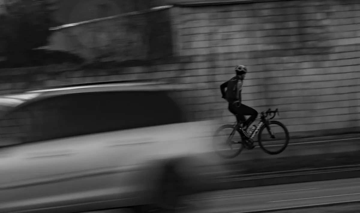 Cyclist in a helmet riding past a blurred white van in black and white